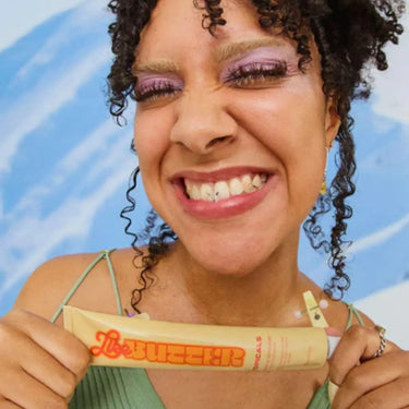 Facial moisturizer Like Butter held by smiling woman with curly hair and colorful eyeshadow